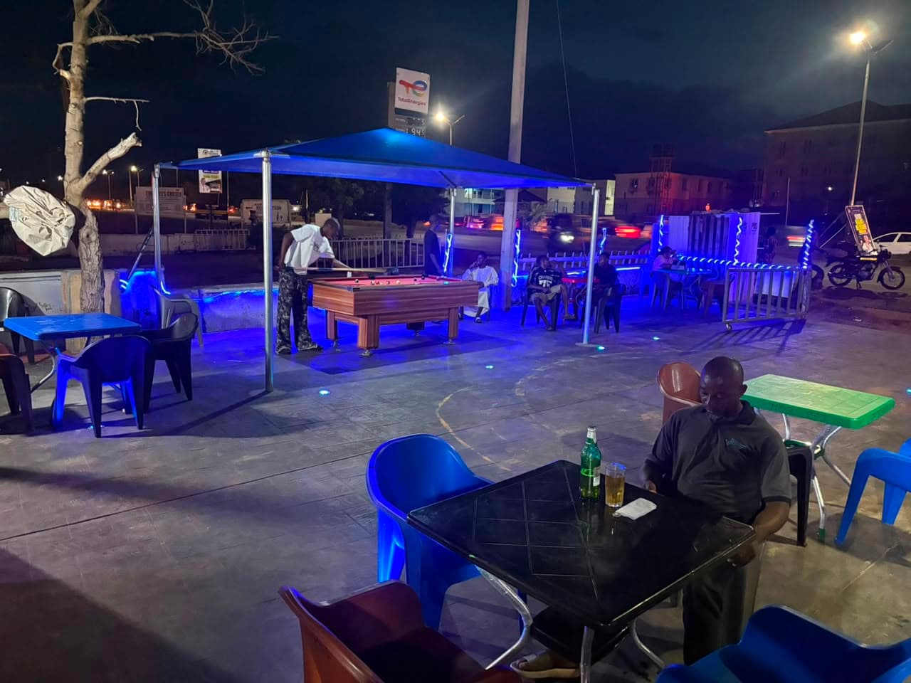 Guests at outdoor tables under the canopy at night with the pool table in the forecourt